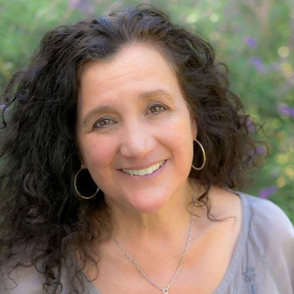 Eve Decker. Woman with dark hair, smiling with greenery in the background.