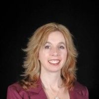 Liesl Piotti. Woman with blonde hair smiles in a maroon jacket against a black background.