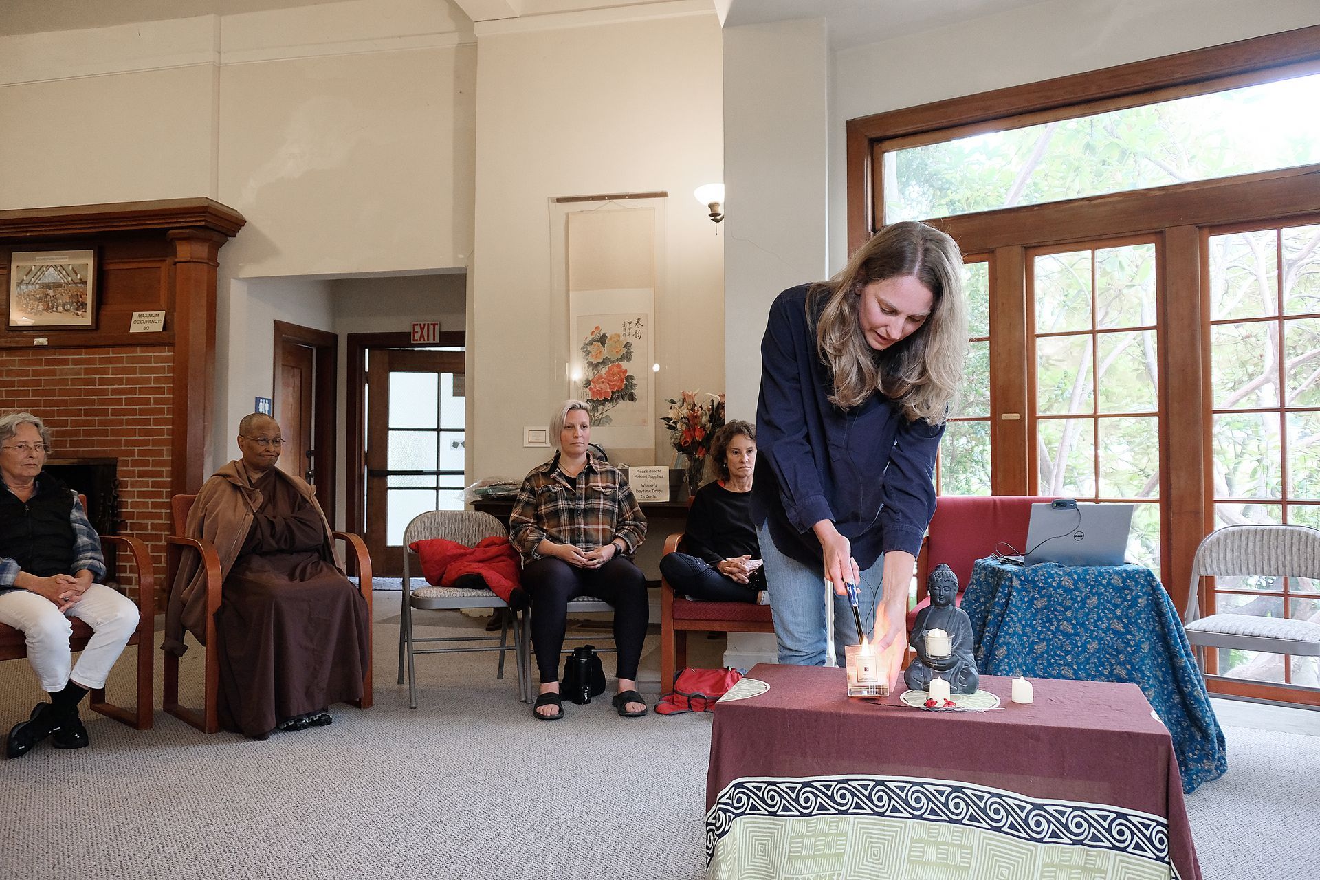 A woman lighting candles at a table, with a group of people watching indoors.