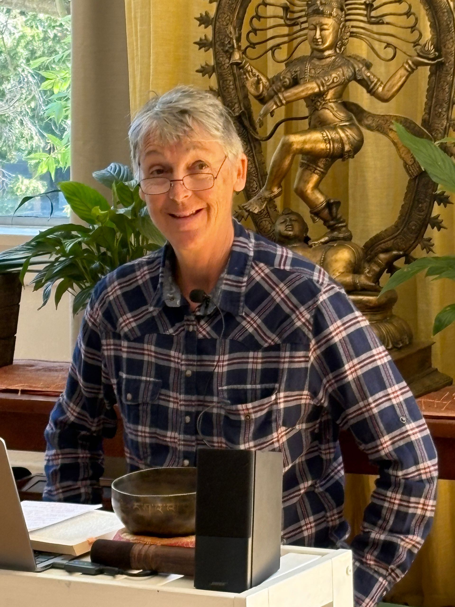 Man in blue plaid shirt smiling, with statue of a dancing figure in background.