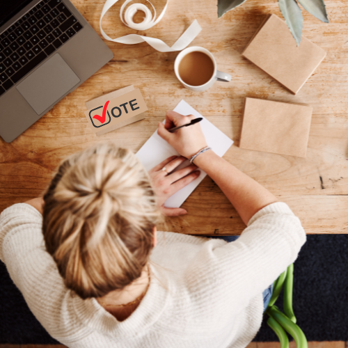 Woman writing at a desk with a laptop and coffee cup. A