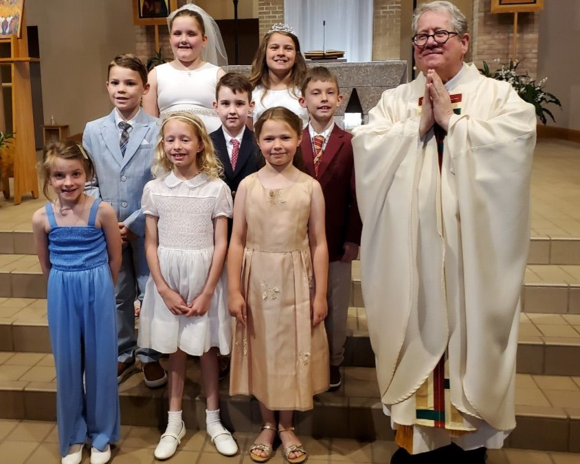 Christ the King First Communicants smiling with Fr. Erich in front of the altar.