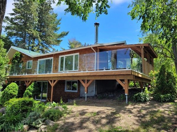 Une maison avec une grande terrasse avec rampe vitrée est entourée d'arbres.