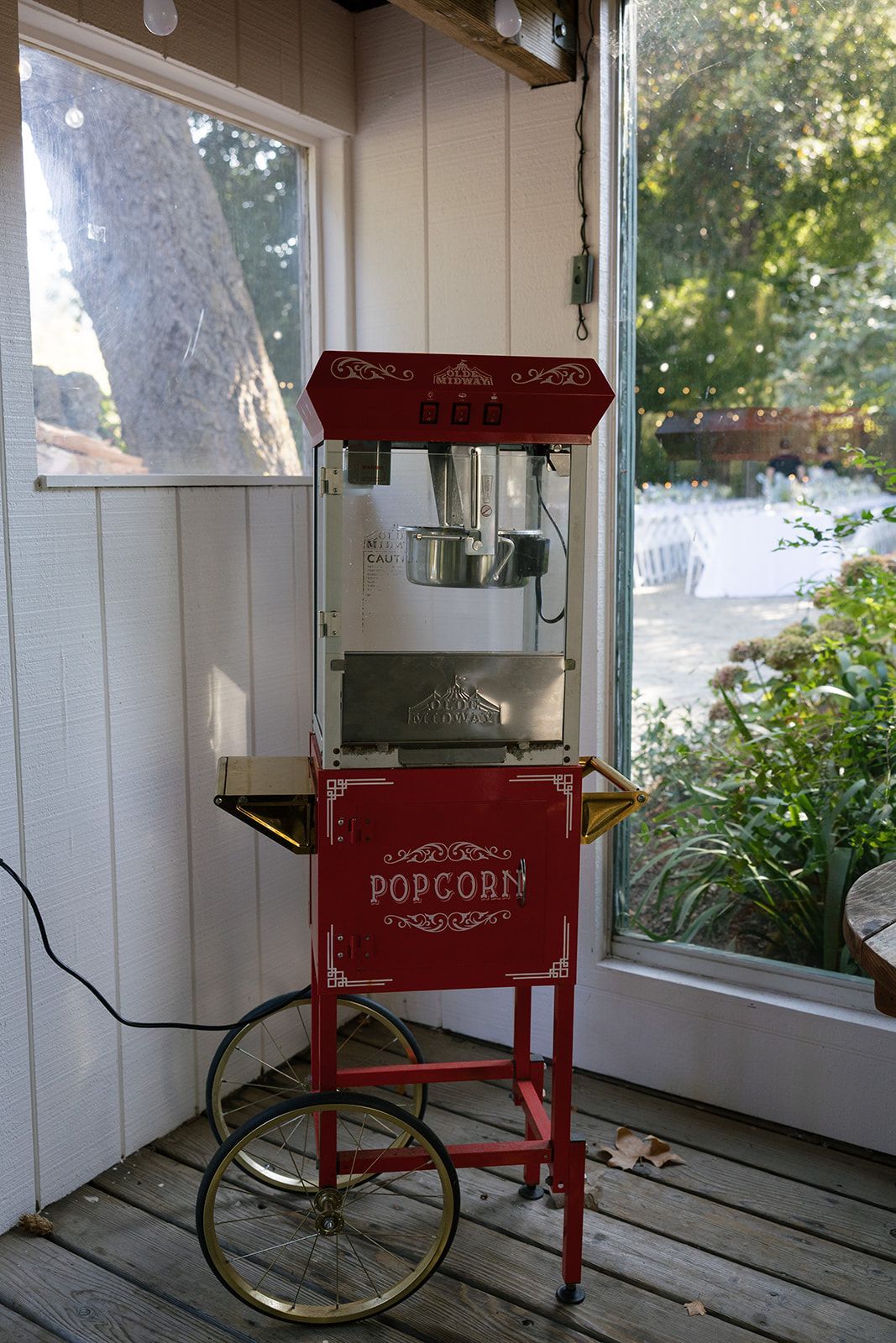 Red popcorn machine on a cart, indoors near a window.