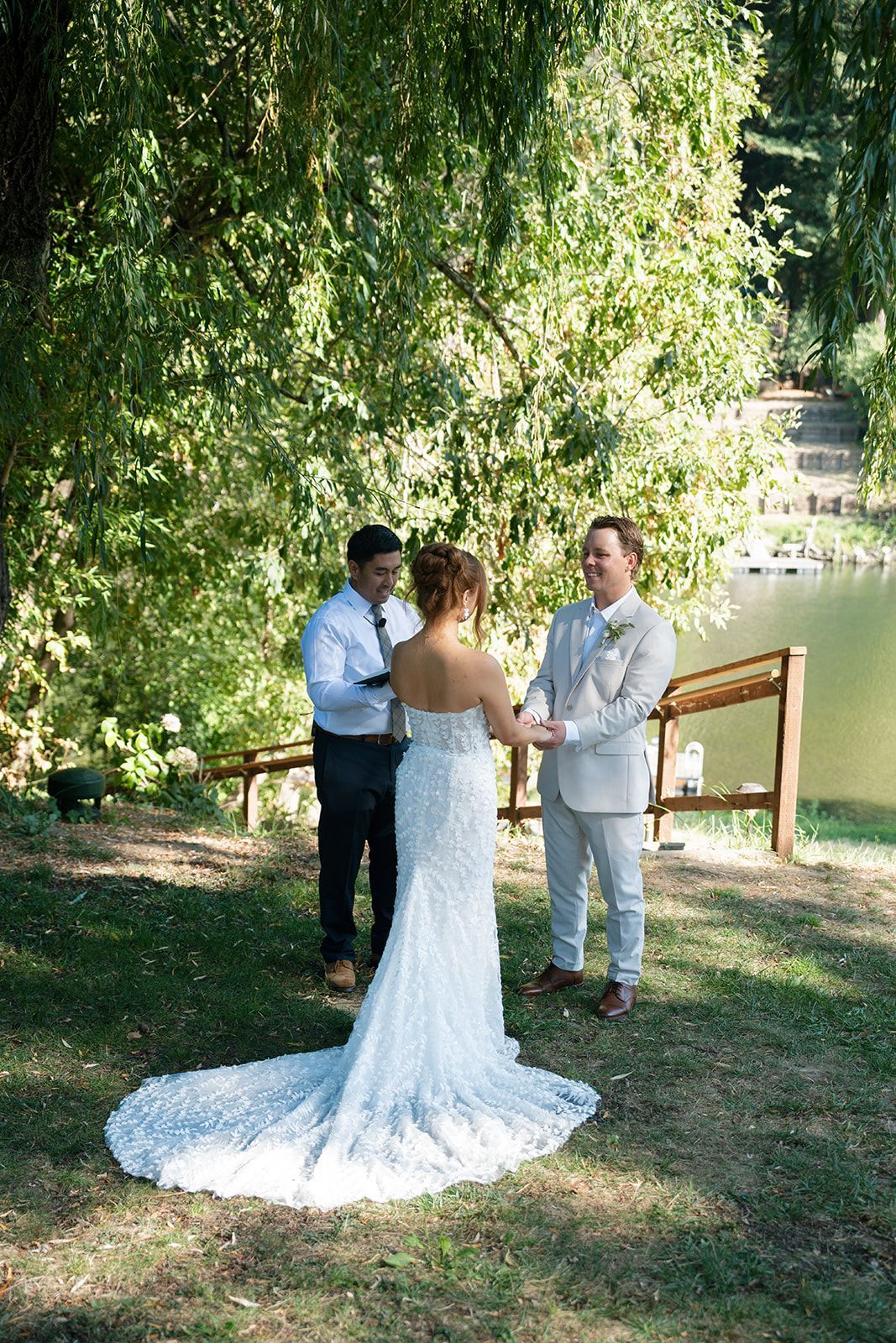 Bride and groom at outdoor wedding ceremony by a lake. Groom in light suit, bride in white dress, officiant.