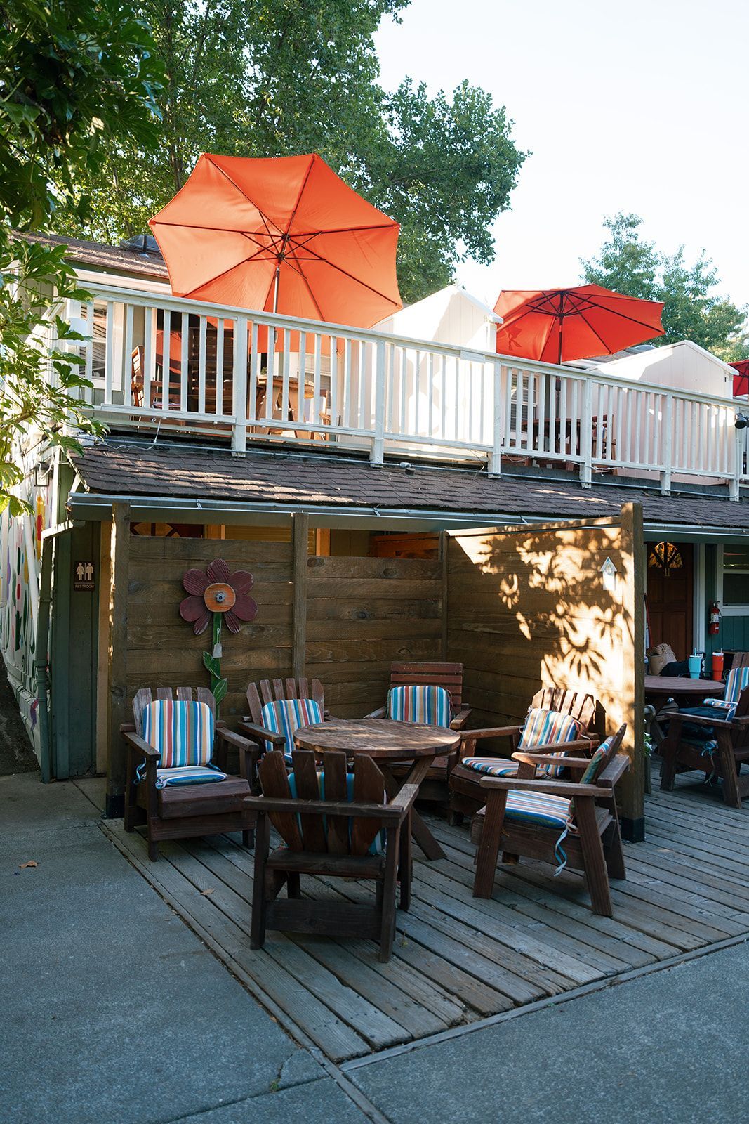 Outdoor restaurant patio with wood furniture, umbrellas, and upper deck.