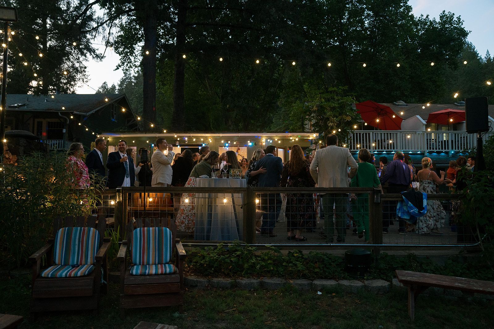 Outdoor gathering with string lights, people, deck, and chairs.