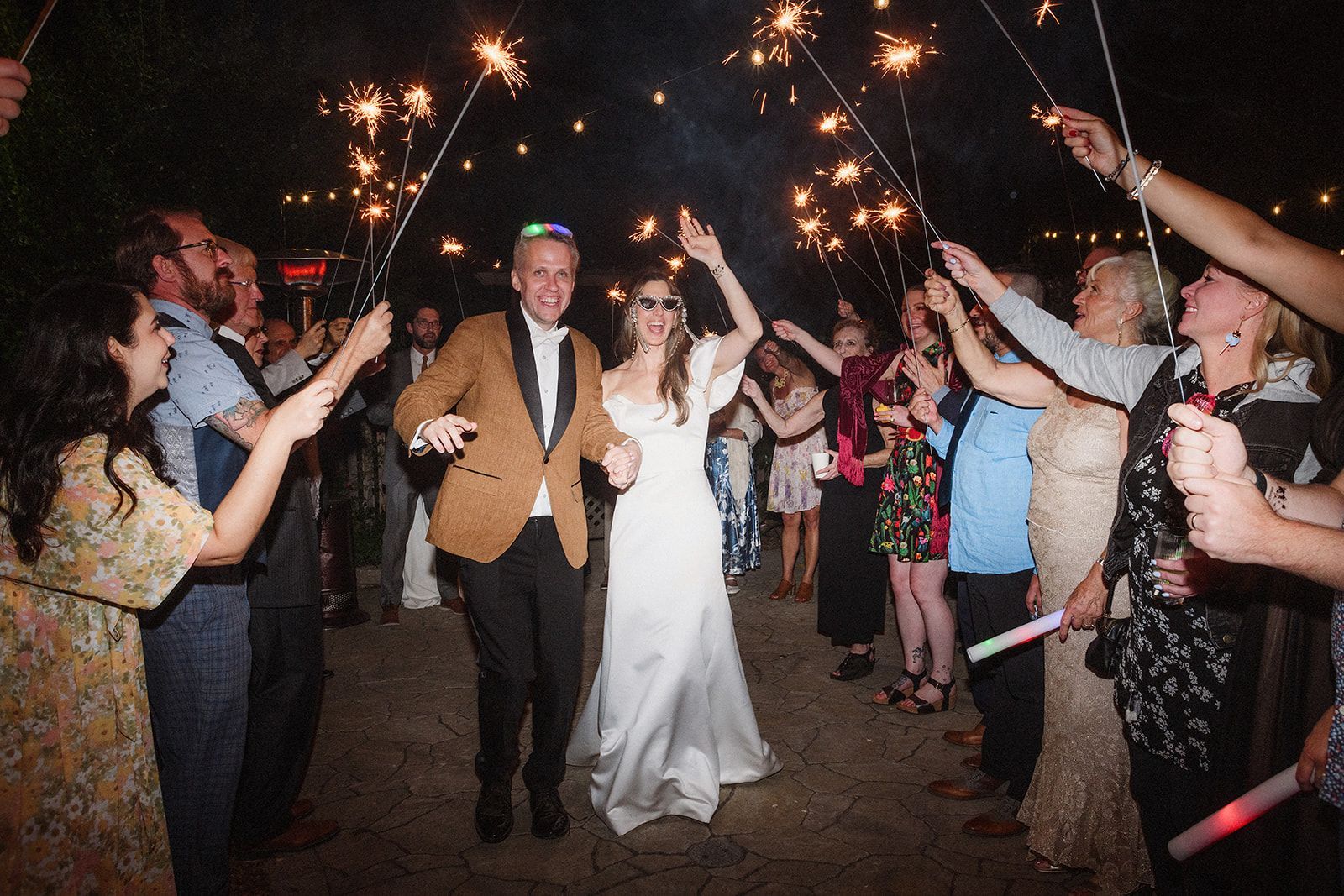 A newly married couple walks through friends with raised hands out on the terrace