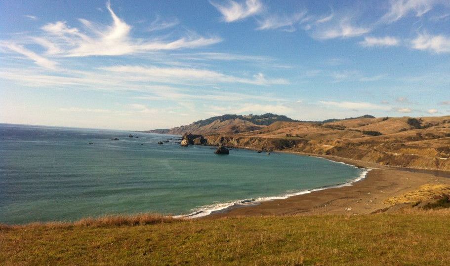 A large body of water surrounded by mountains and grass on a sunny day.