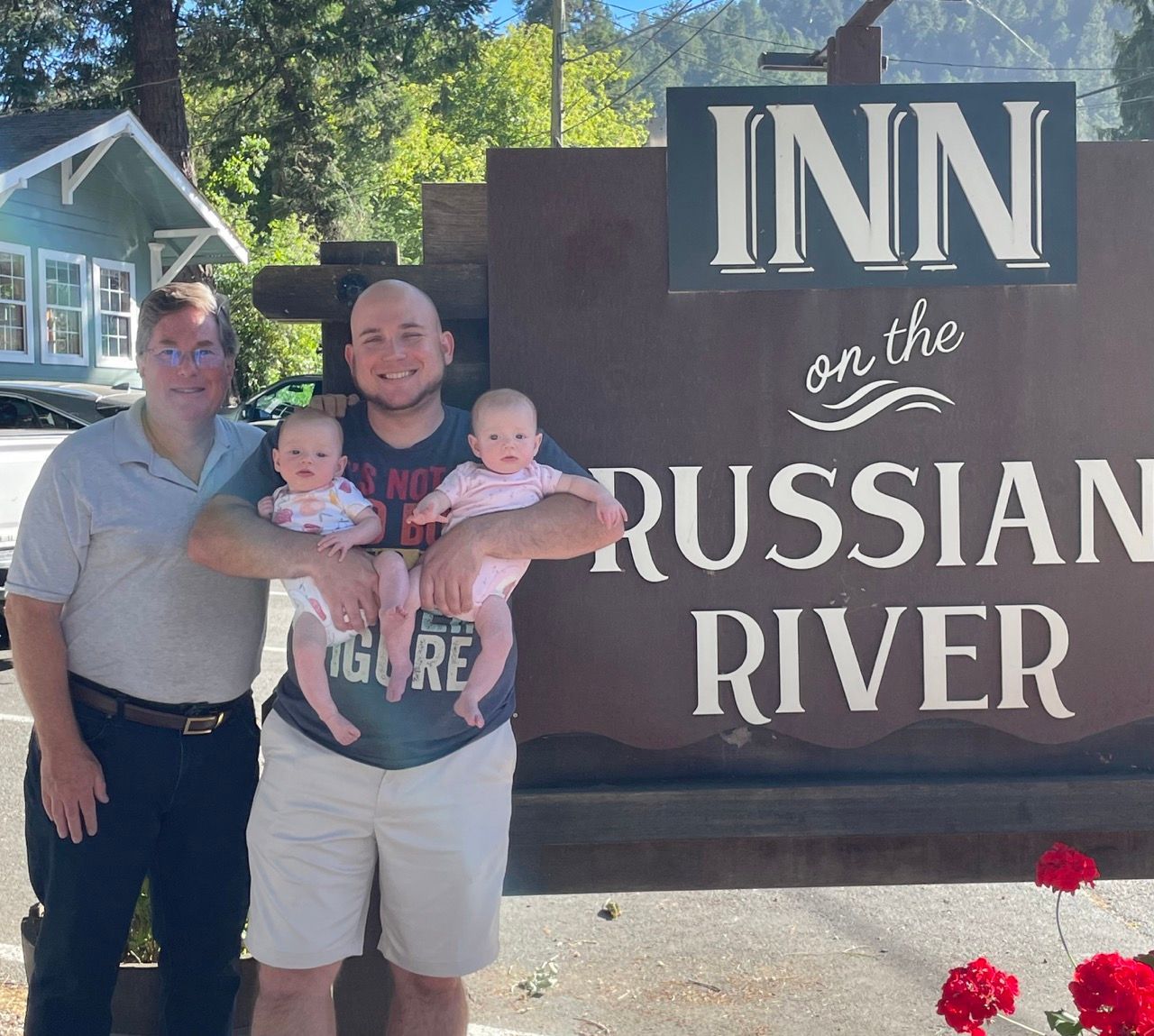 Two gay men with twin babies in front of a sign for 