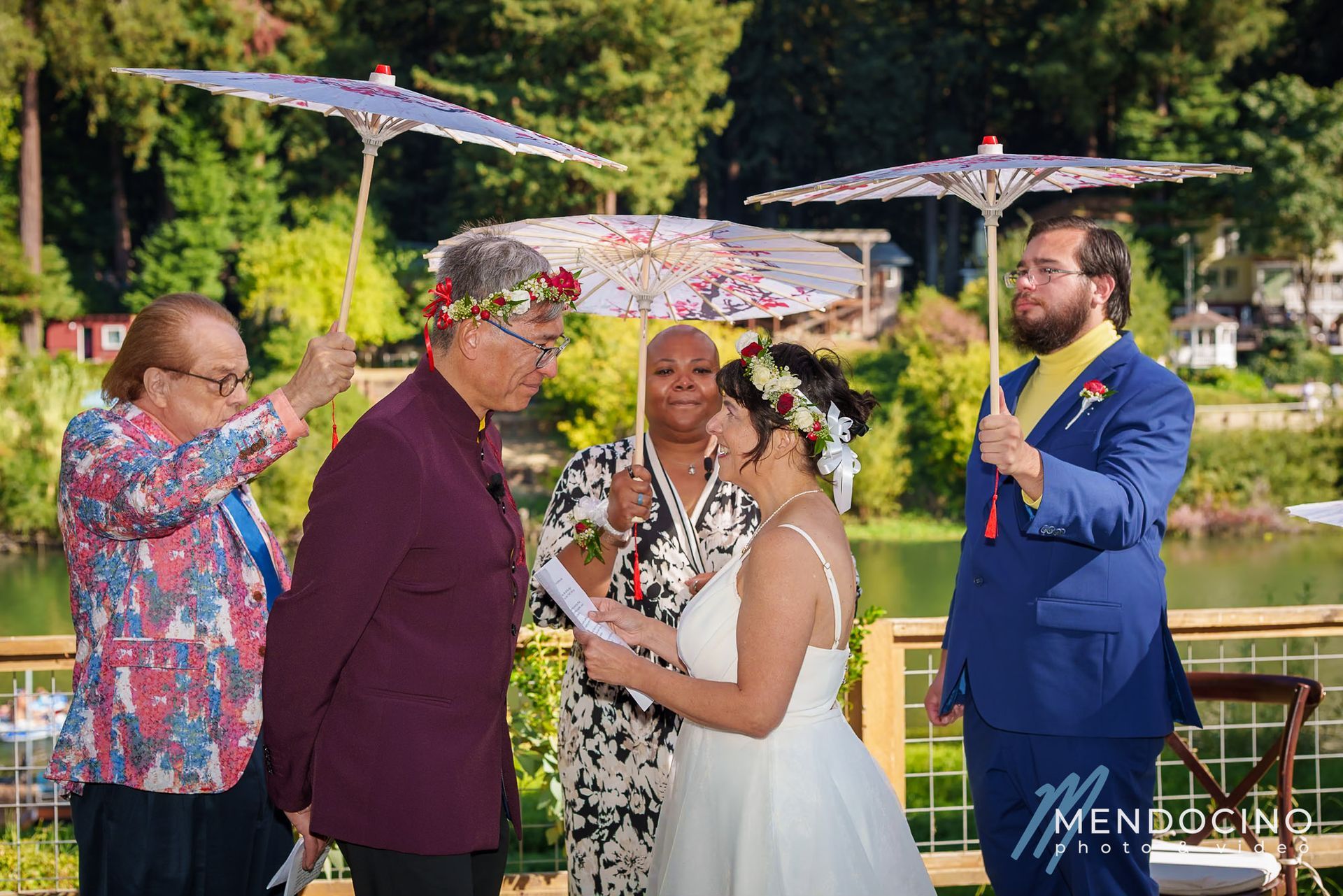 A wedding couple reads vows to each other under parasols with the Russian River in the background