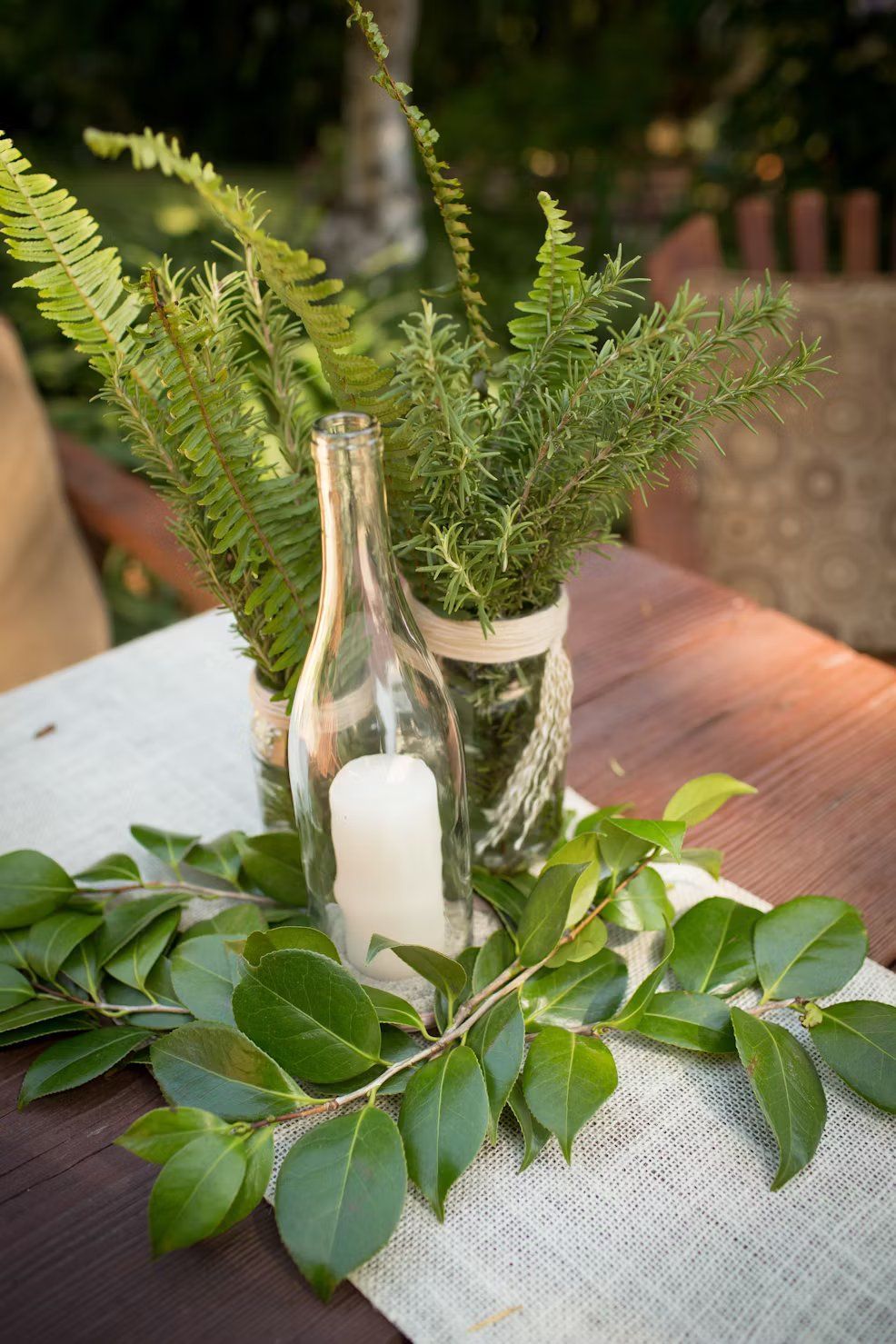A table with a vase filled with greenery and a candle on it.