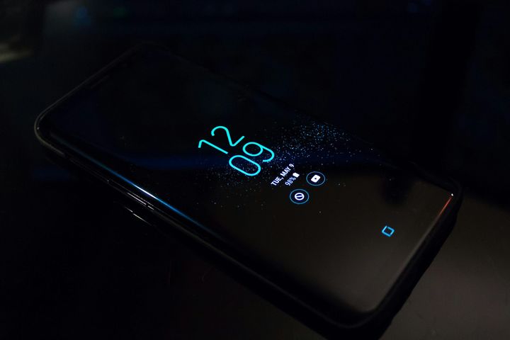 Black smartphone, with lit up display showing time and weather icons.