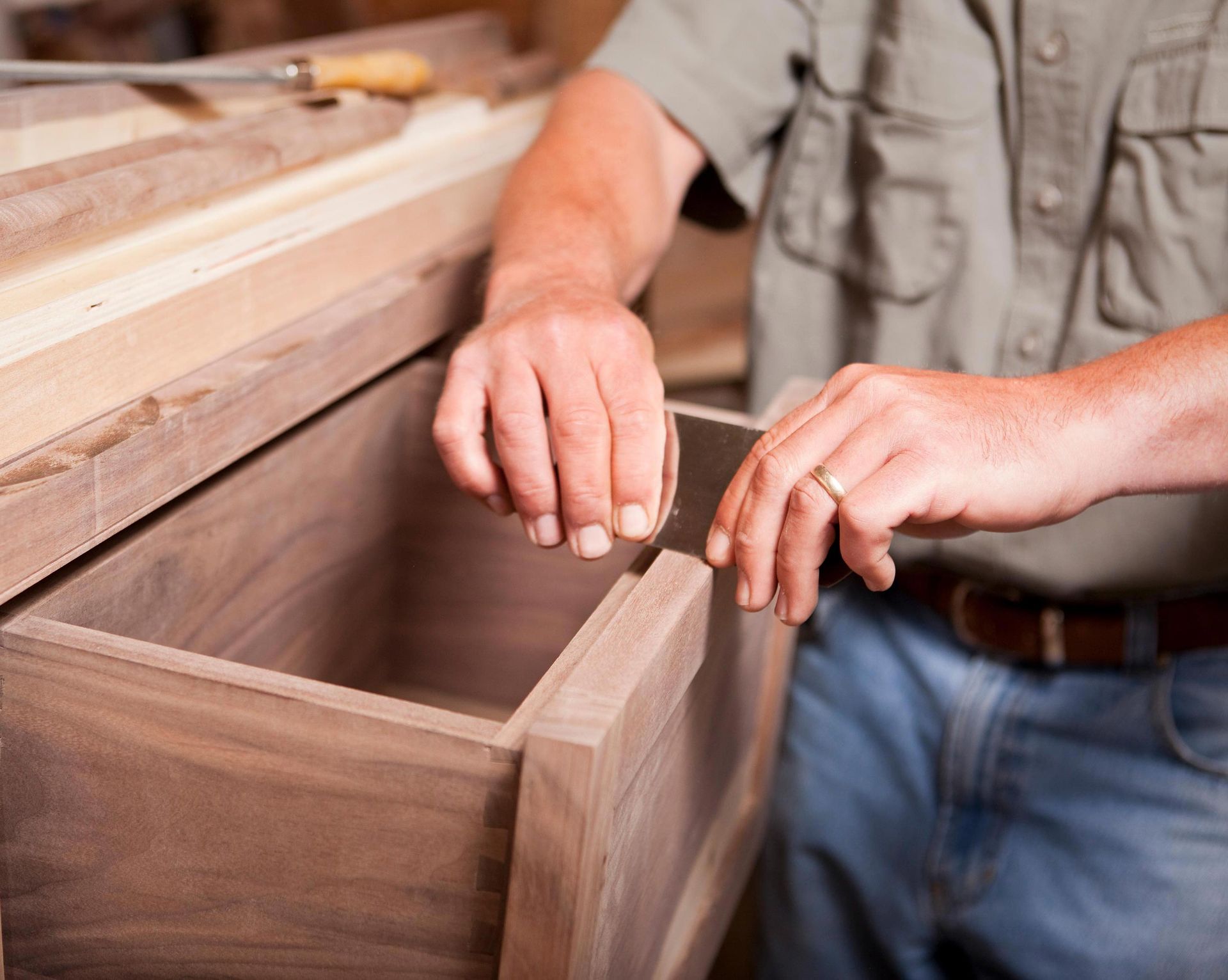 Woodworker assembling a wooden drawer in a workshop, wearing jeans and a light shirt.