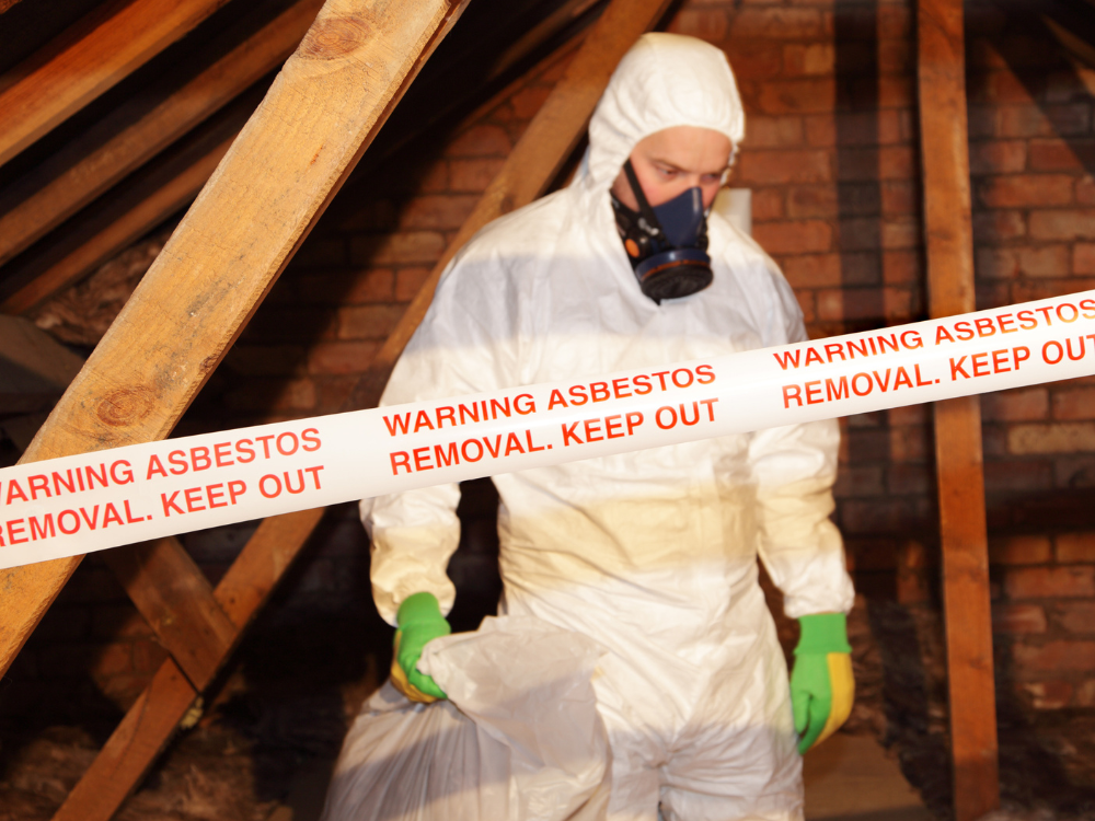 A person in a hazmat suit within a building removing asbestos and other hazardous material.
