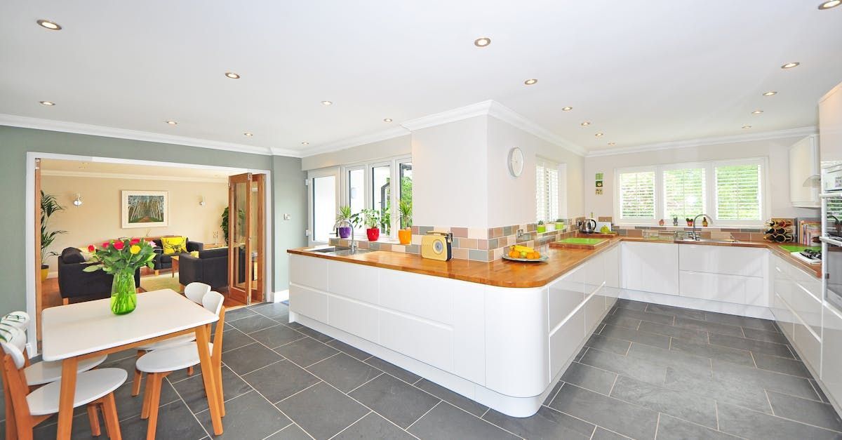 A kitchen with a table and chairs in it and a living room in the background.