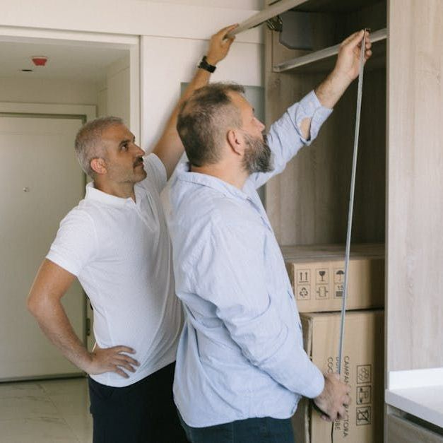 Two men are measuring a shelf with a tape measure.