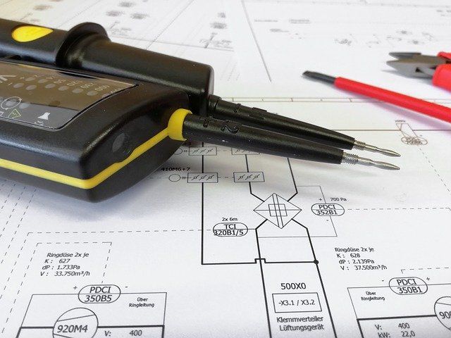 Multimètre avec sondes sur plan, accompagné d'une pince et d'un tournevis.