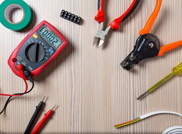 Outils électriques, dont un multimètre, des pinces à dénuder et des pinces, disposés sur une surface en bois.