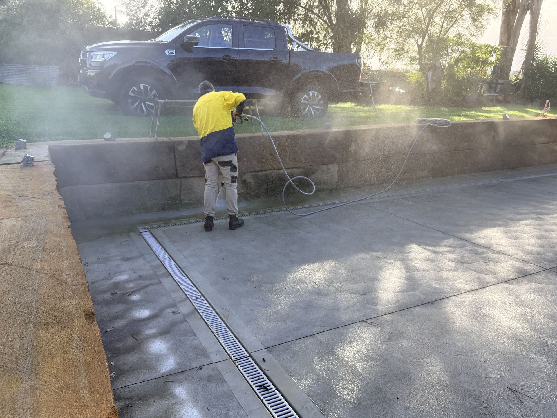 Person in a yellow shirt pressure-washing a concrete driveway near a parked black truck