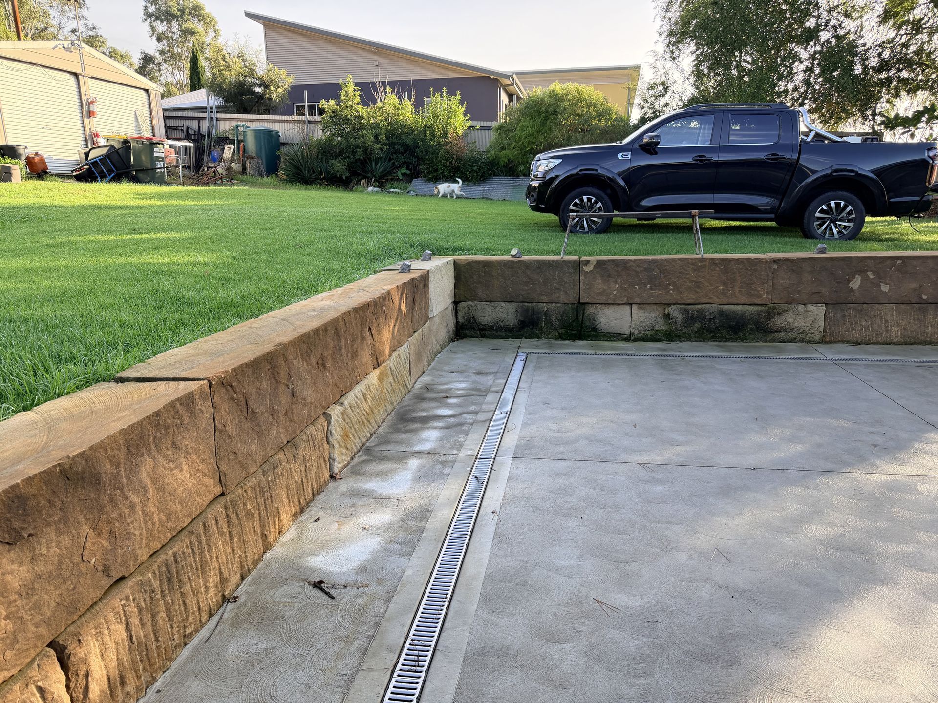 Concrete parking area beside a grassy yard, with a black pickup truck parked on the far side.