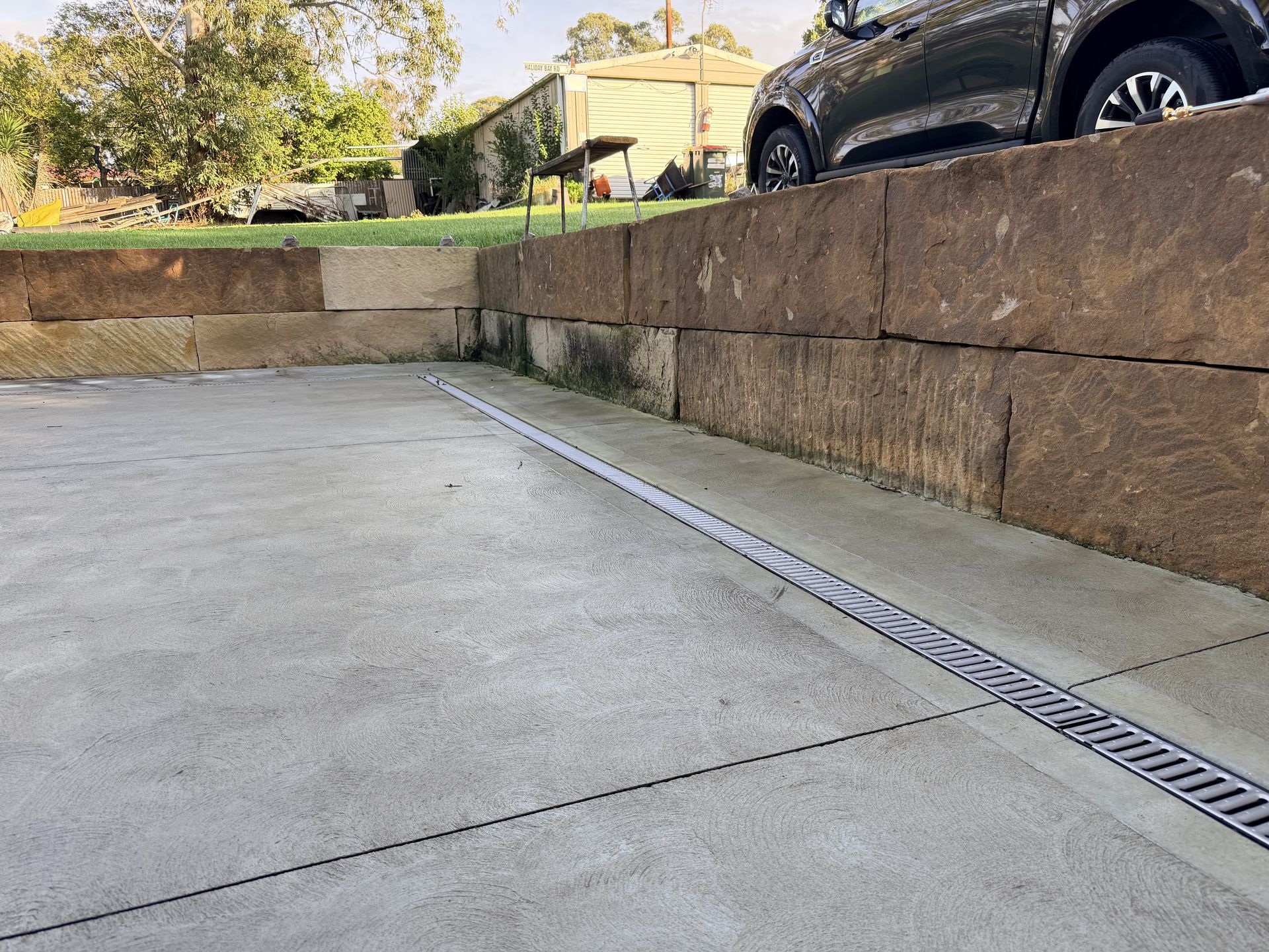 Low concrete driveway with stone retaining wall and parked car above it