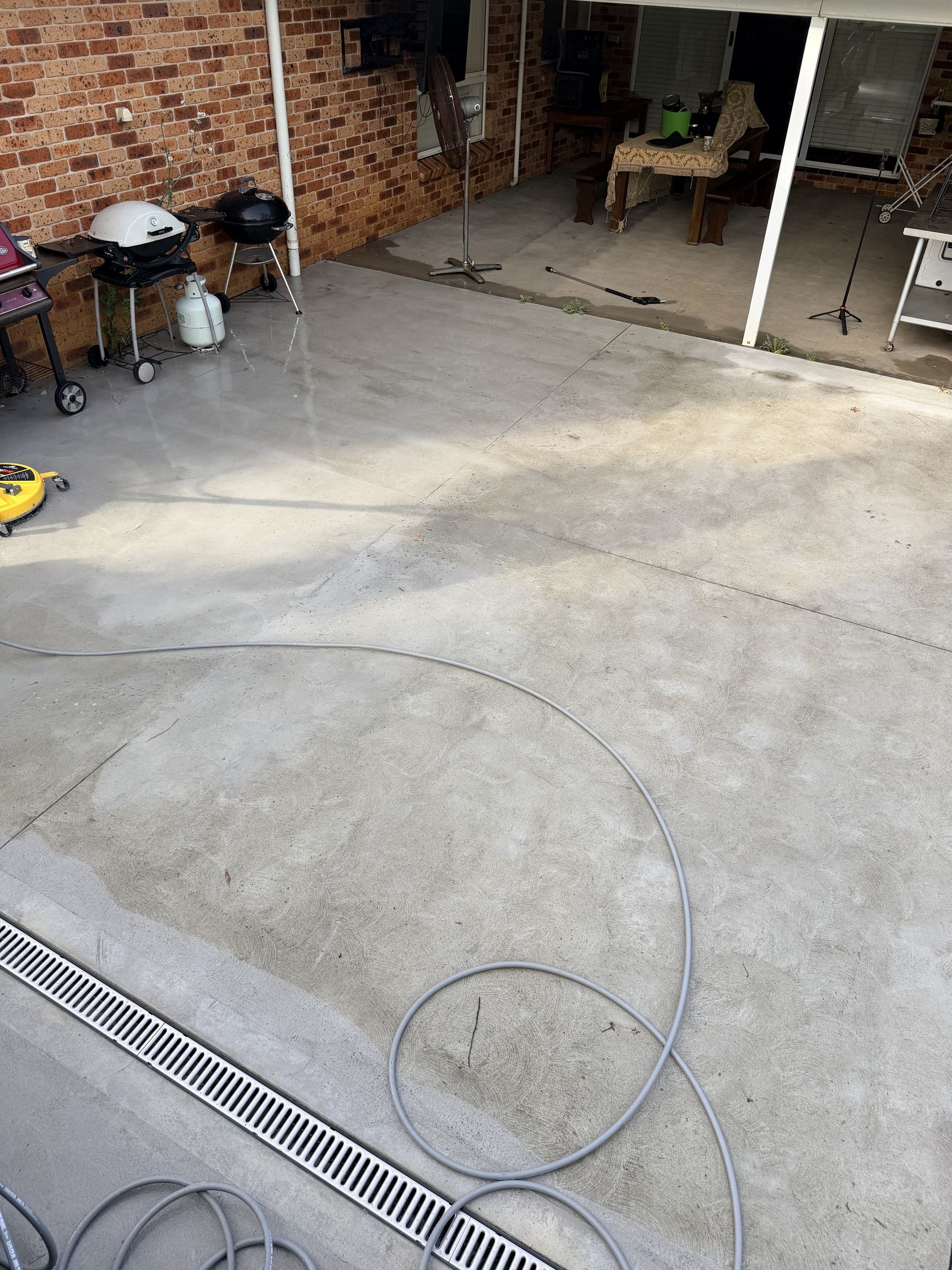 Concrete patio with brick wall, grill, table, and a garden hose on the ground