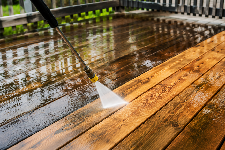 Pressure washer spraying a black wall beside a wheeled cleaning machine and yellow hose