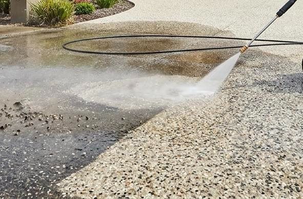 Pressure washing a concrete driveway, spraying dirt and water across the surface