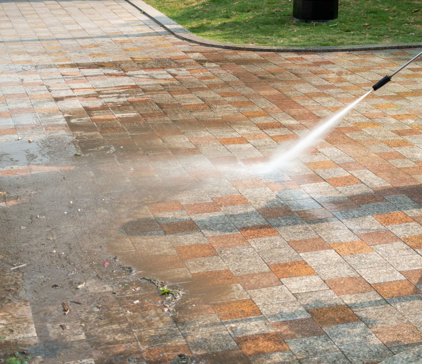 Pressure washing a brick walkway, spraying water and cleaning dirty tiles