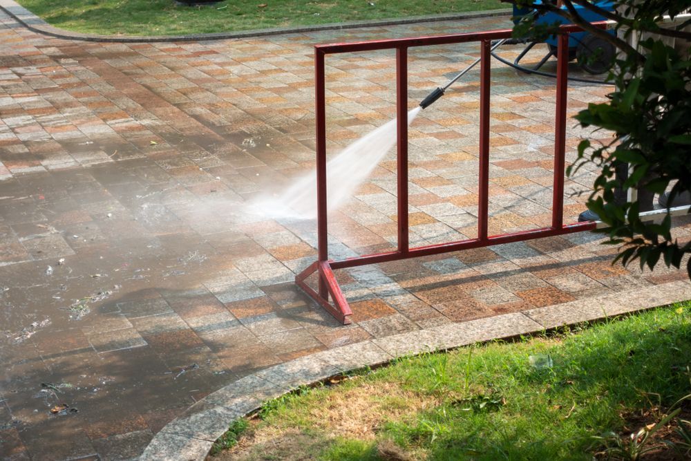 Water spraying from a broken pipe near a red metal gate on a wet sidewalk.