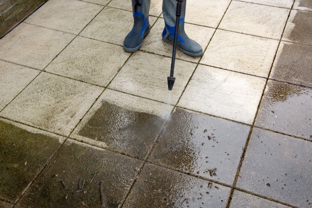 Person wearing blue boots pressure-washing wet stone paving slabs