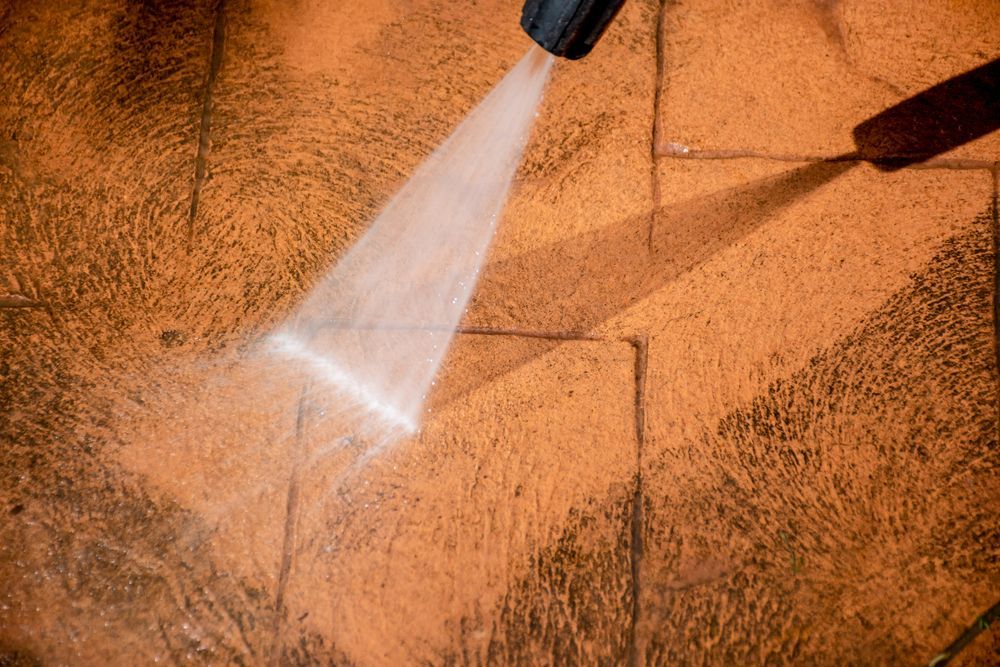 Person pressure-washing a cobblestone path beside green hedges