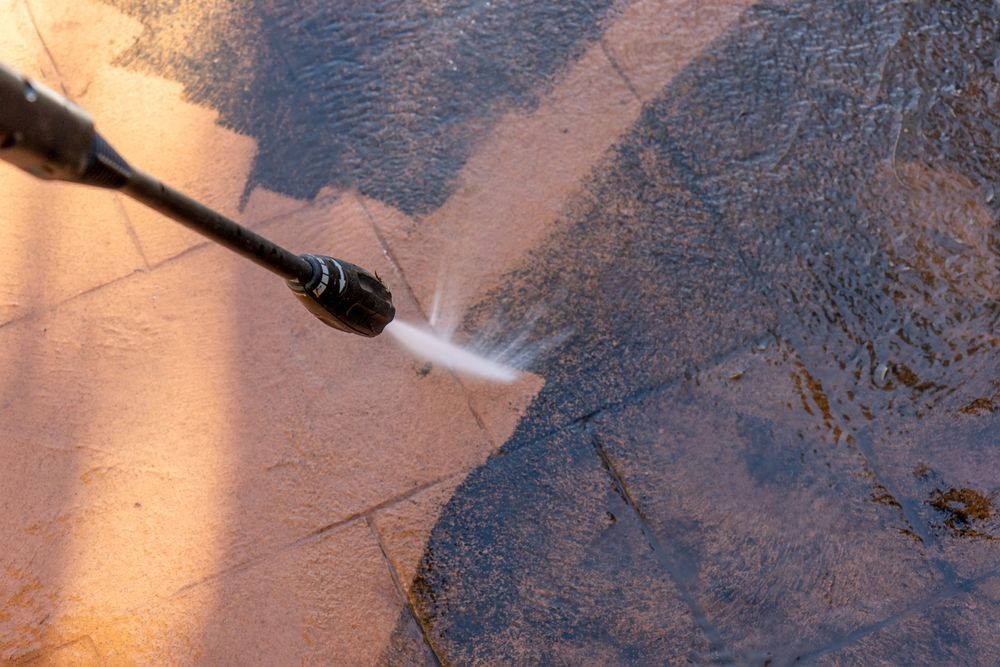 Pressure washer spraying water on a surface, cleaning a tan and blue area.