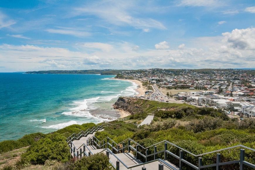 Coastal lookout over turquoise ocean, sandy beach, and a sunlit seaside town under a blue sky