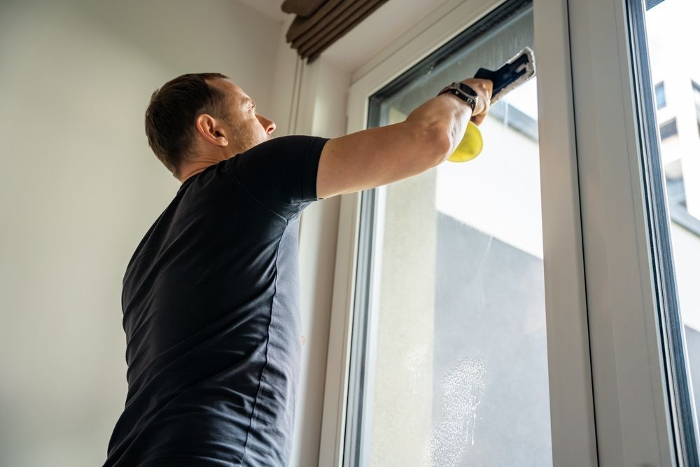 Person cleaning a window with a squeegee, wearing a black shirt indoors