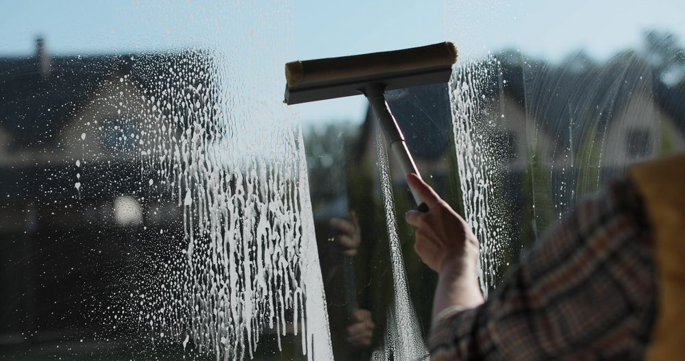 Person cleaning a window with a squeegee, leaving streaks on the glass.