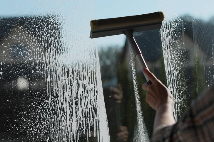 Person using a squeegee to clean a window with water droplets on the glass