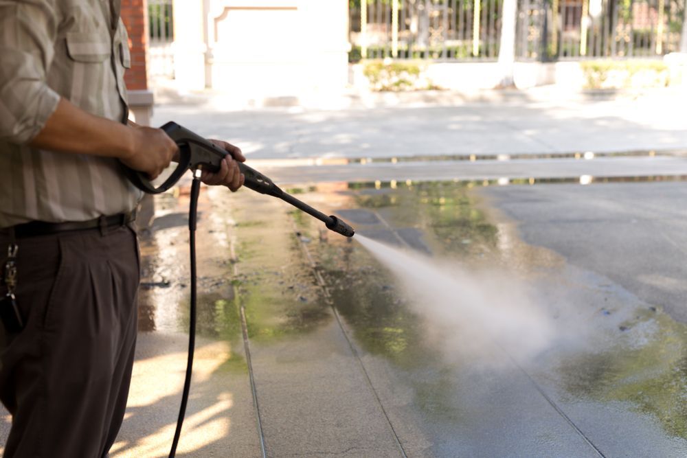 Person pressure-washing a wet sidewalk with a hose nozzle on the left side of the frame