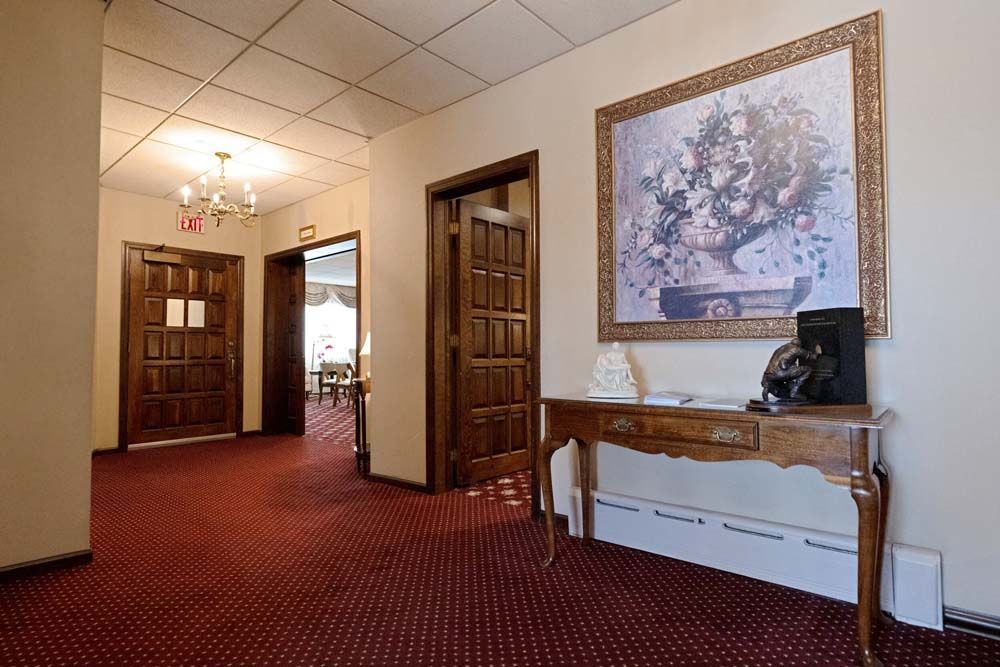 Hallway with red carpet, wood doors, floral art, and a decorative table.