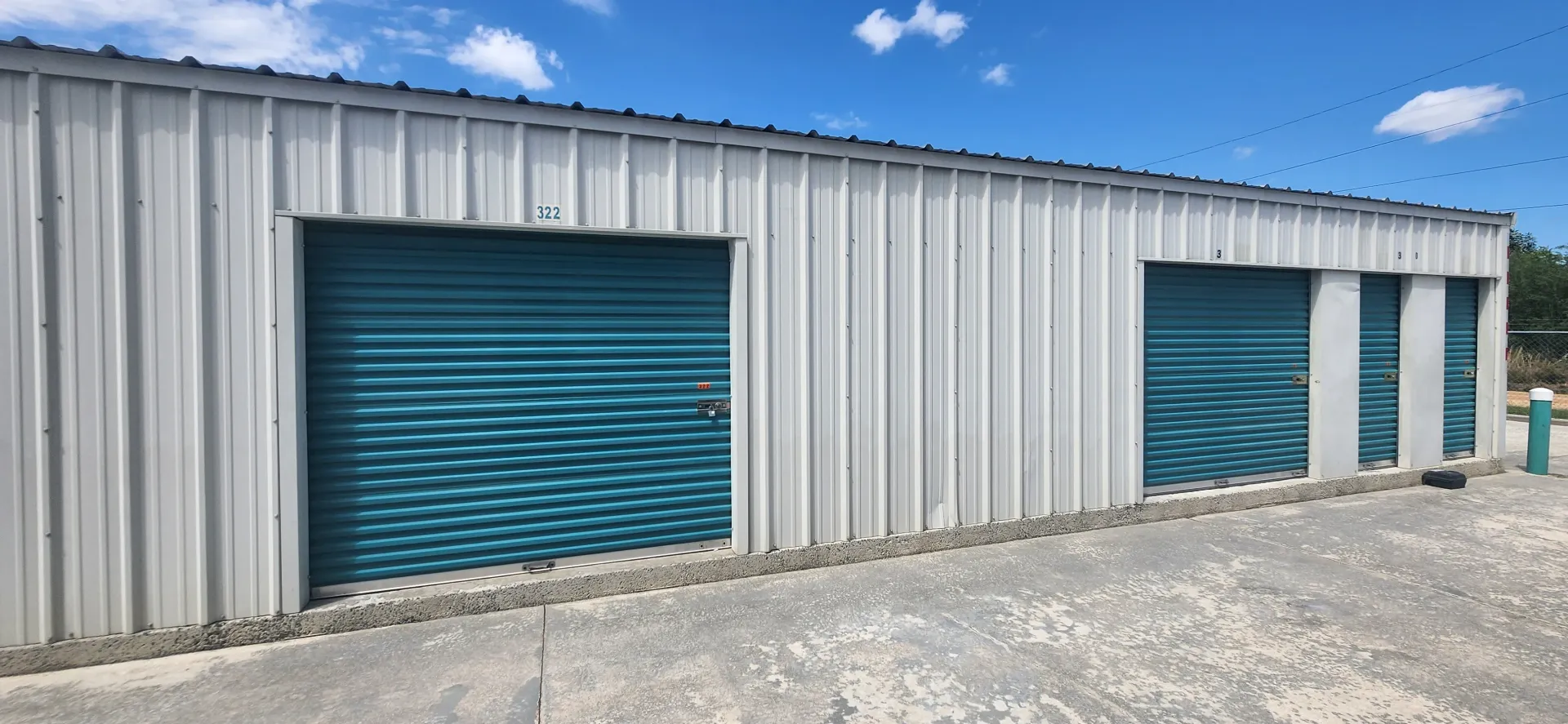 Storage building with teal roll-up doors on a gravel lot under a blue sky