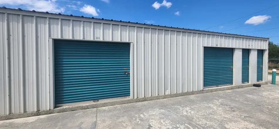 Storage building with teal roll-up doors on a gravel lot under a blue sky