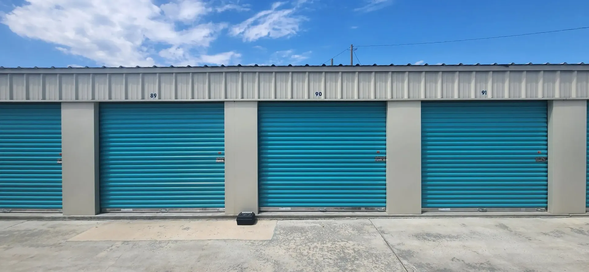 Row of blue storage unit doors on a beige building under a clear sky