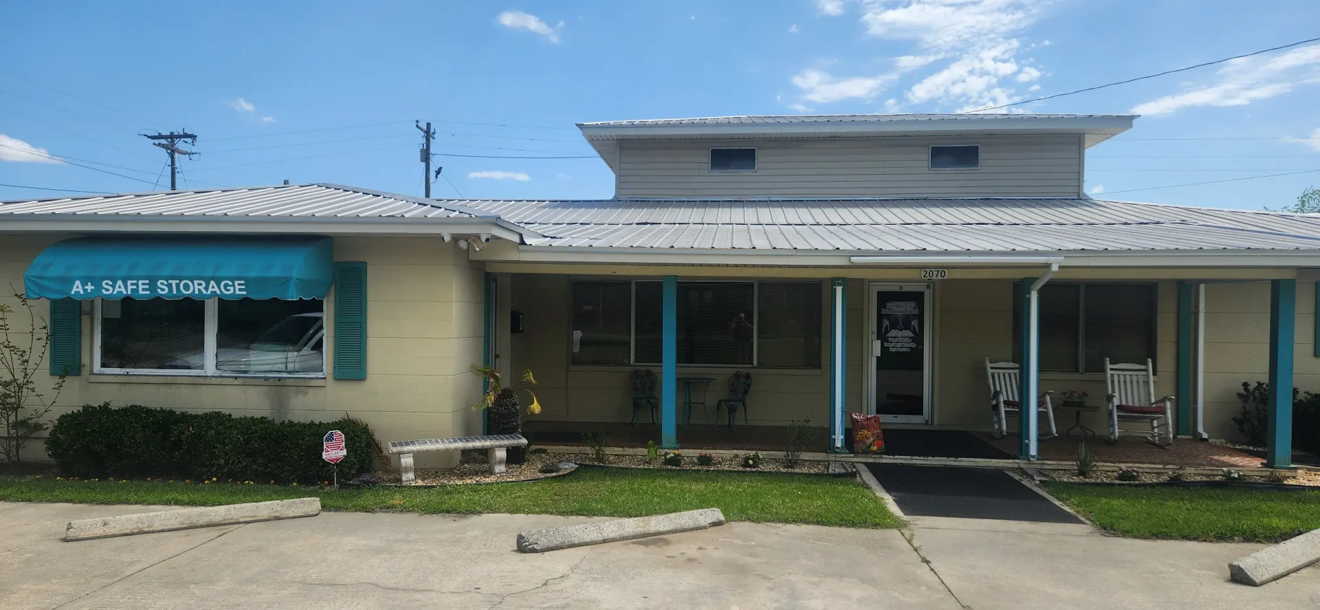 White storage units with teal roll-up doors on a gravel lot under a blue sky