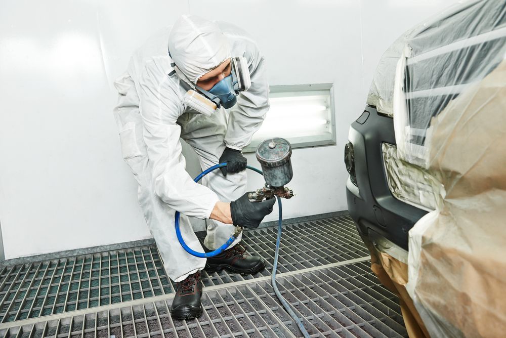 Worker in White Protective Suit Spray-painting a Car in a Body Shop Booth — Jackman's Bodyworks in Huonville, TAS