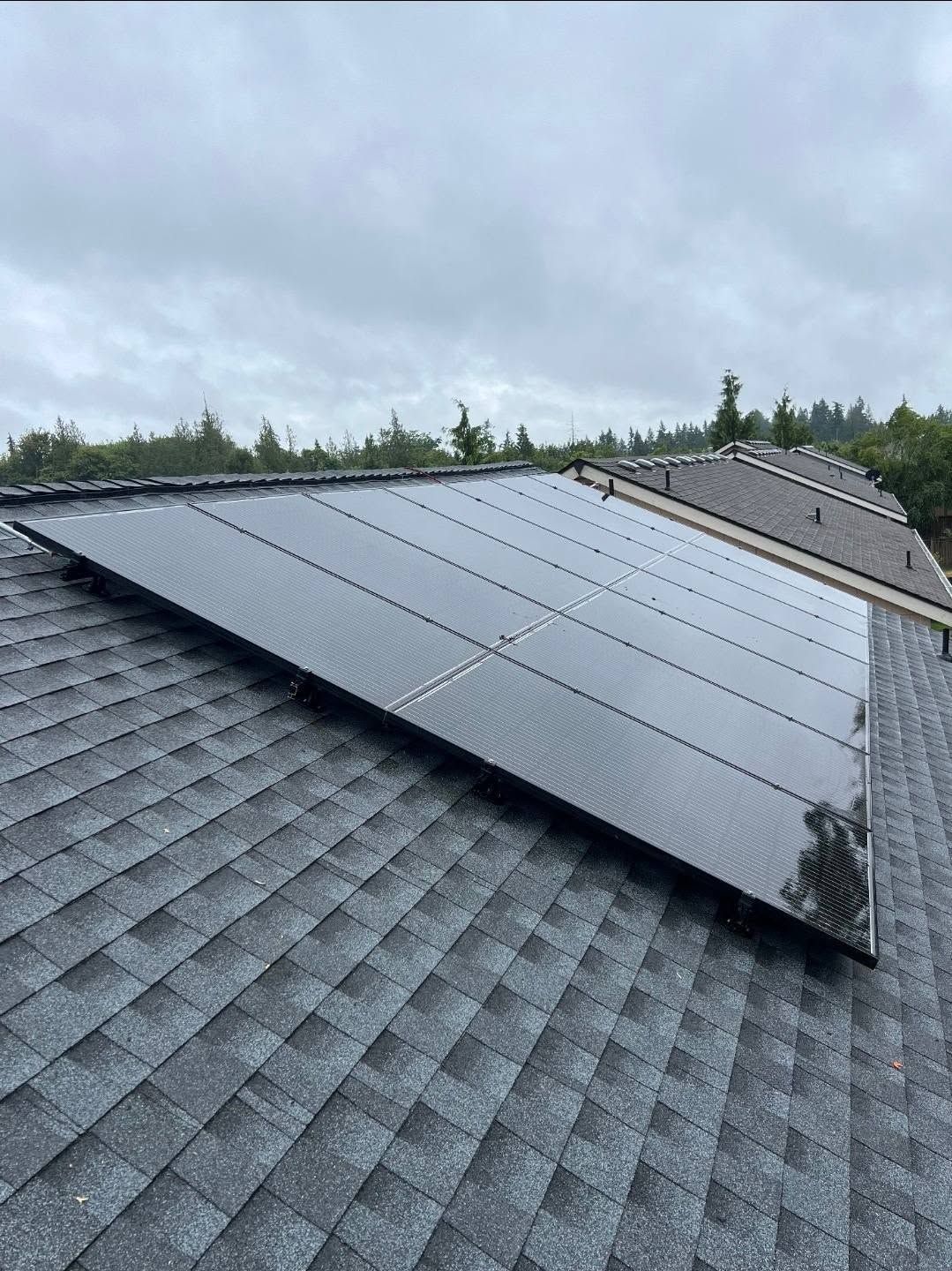 Solar panels mounted on a dark shingled roof under a cloudy sky