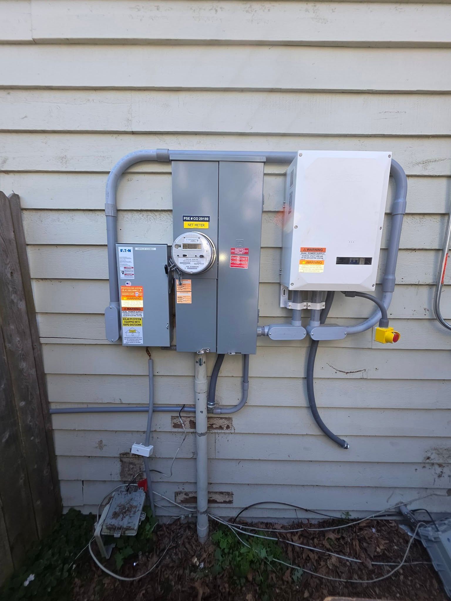 Three utility meters and panels mounted on an exterior house wall with conduit and cables.