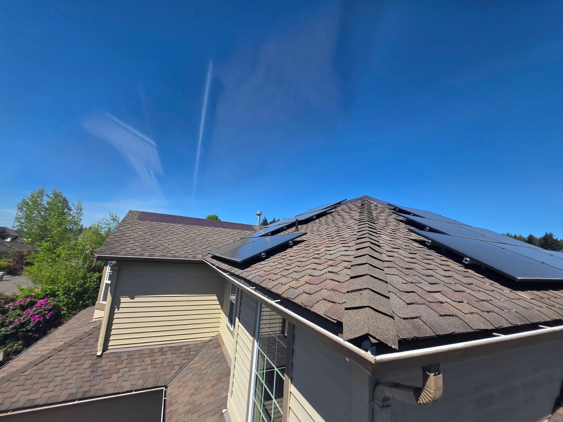 Roof with blue solar panels under a clear blue sky, viewed from above a house.