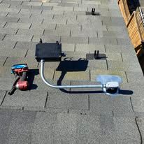Shingled rooftop with a red blower, black vent box, and silver duct connected to a white vent hood.
