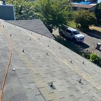 Rooftop with multiple small fixtures, a white truck parked below, and trees along a sunny residential street.